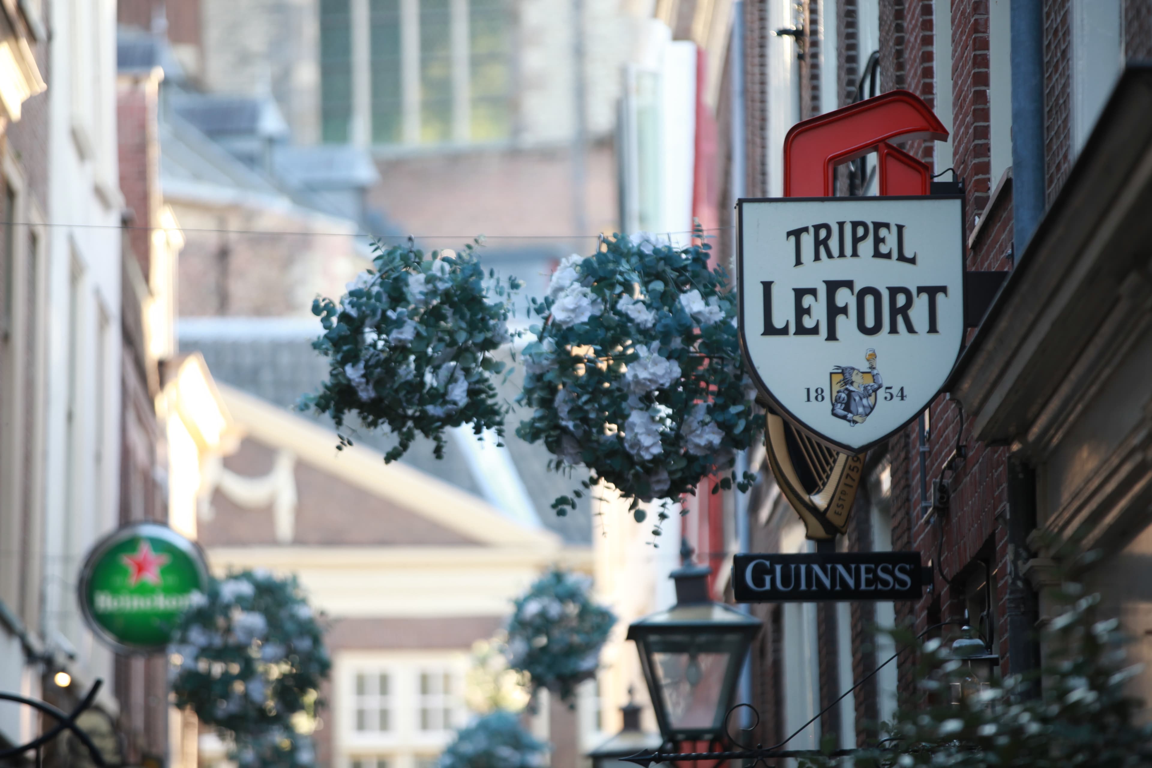 Historic pub signs and flower baskets on a narrow Leiden street
