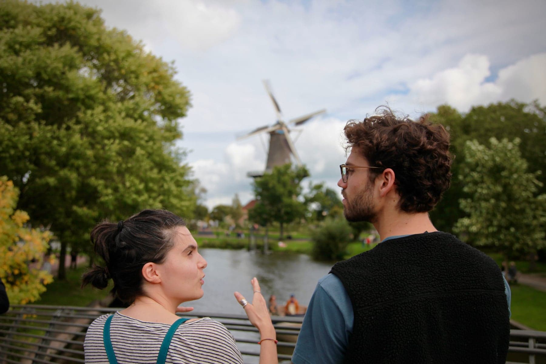 Two people talking beside a Leiden canal with a windmill in the background